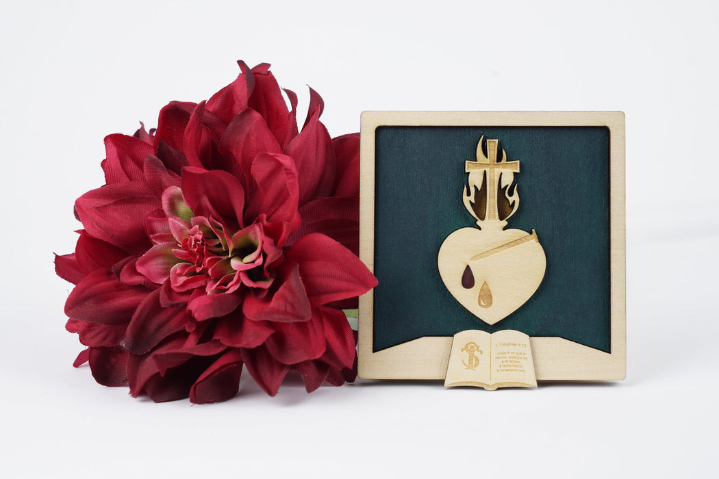 Cadre chrétien Sacré-Cœur de Paray-le-Monial en tilleul massif - Flammes dorées et couronne d'épines. Le fond est vert émeraude. Le cœur est traversé par un clou. Le cœur porte deux gouttes : une goutte de sueur gravée et une goutte de sang, peinte en rouge. Le feu qui entoure la croix positionnée sur le cœur est entouré de flammes dorées