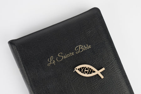 Pendentif poisson déposé sur une bible noire avec l'inscription "La Sainte Bible"